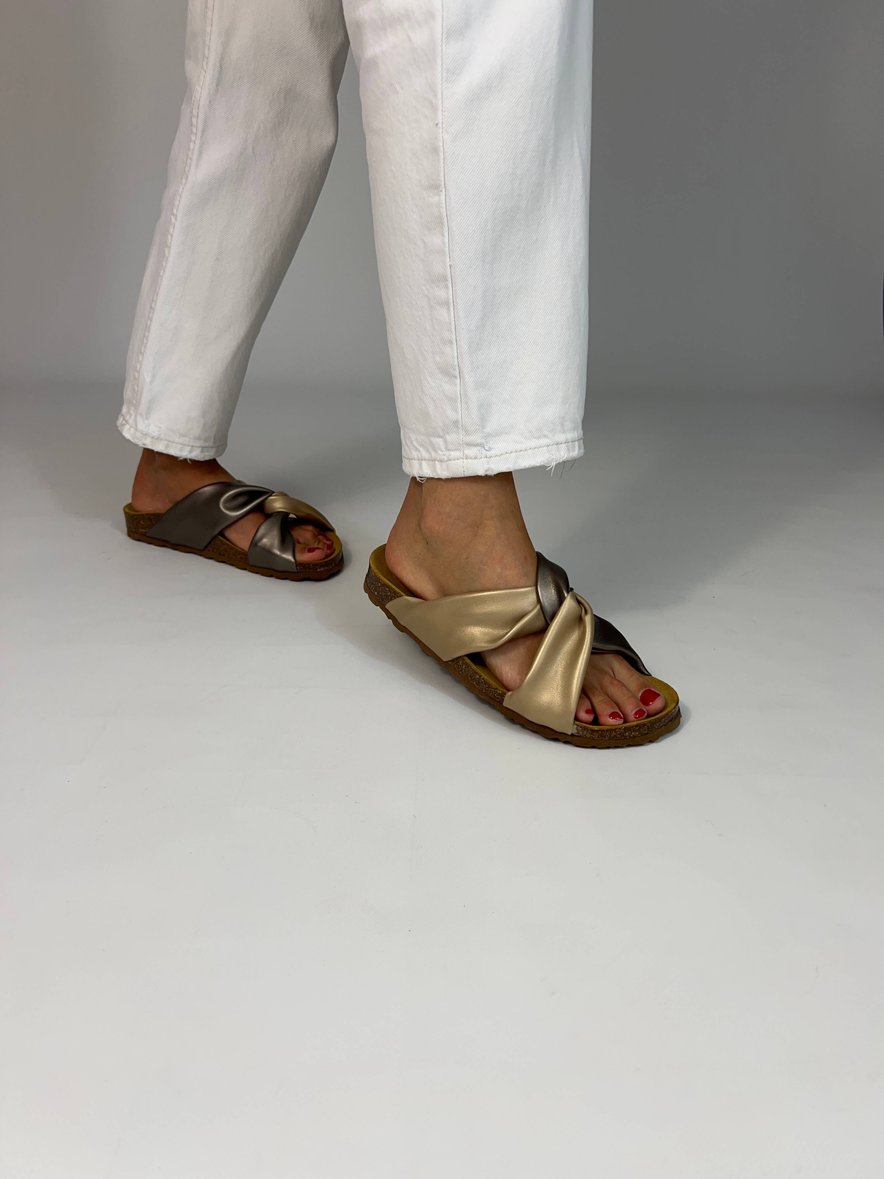 Momoc Calpe bronze champagne metallic sandals worn side view white trousers cross strap design | Momoc Shoes Spain