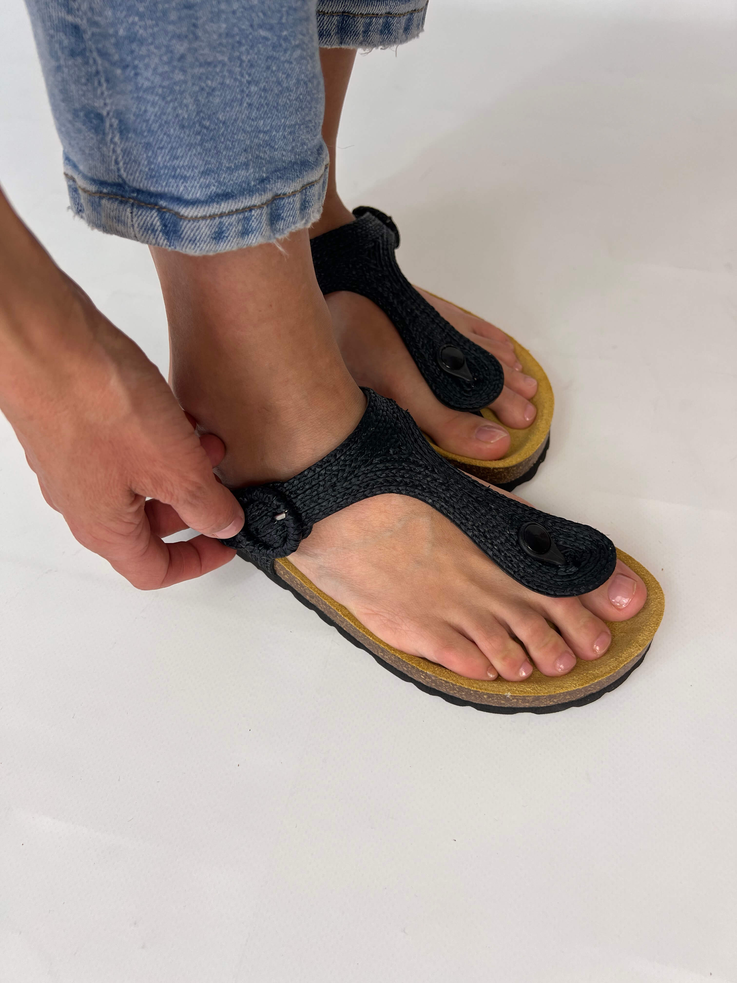 Momoc Altea black raffia sandal close up hand adjusting raffia buckle detail Spain | Momoc Shoes