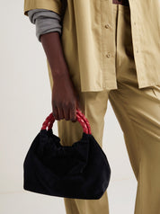 Momoc Pigalle black velvet bag burgundy handle held by hand beige outfit side view | Momoc Shoes